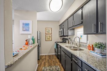 A kitchen with vinyl plank flooring and granite counter tops and dark cabinets at 701 south apartments in mobile, al